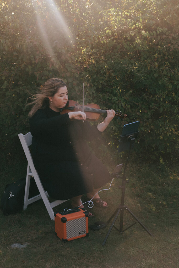 Breeze blows through the solo violinist's hair as she plays music for the wedding ceremony at Castle Hill Lighthouse. Photo by Rhode Tripper Photography