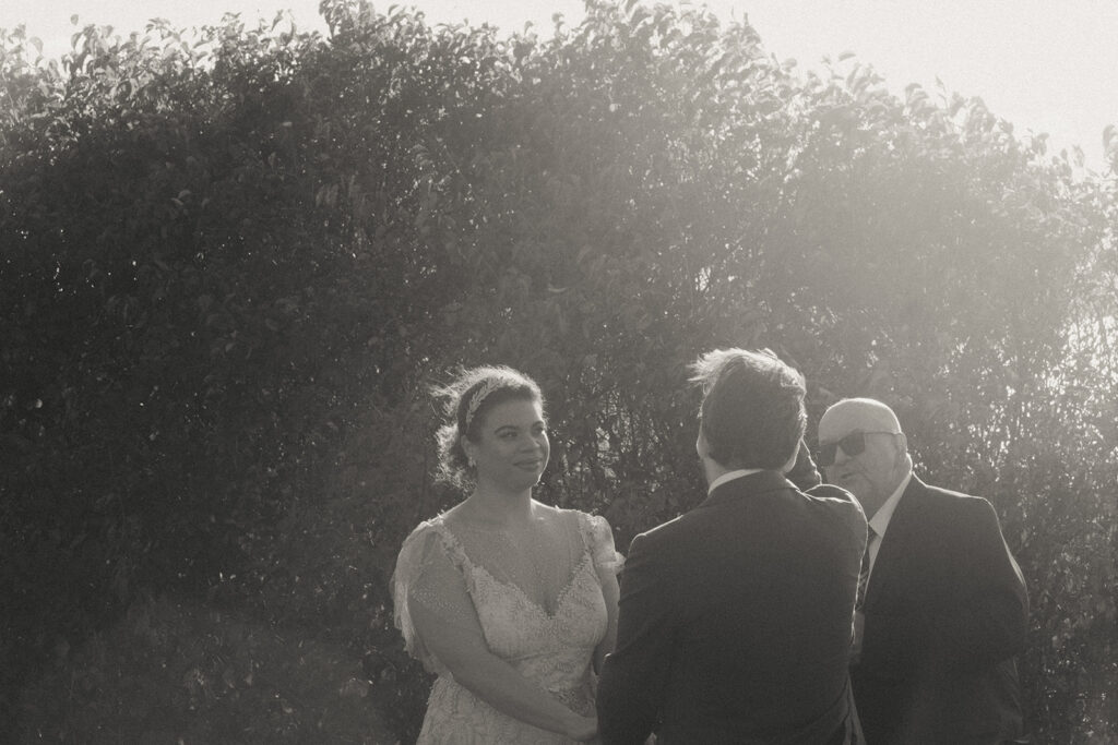 Black and white photo of couple at their wedding ceremony with sun flare. Photo by Rhode Tripper Photography