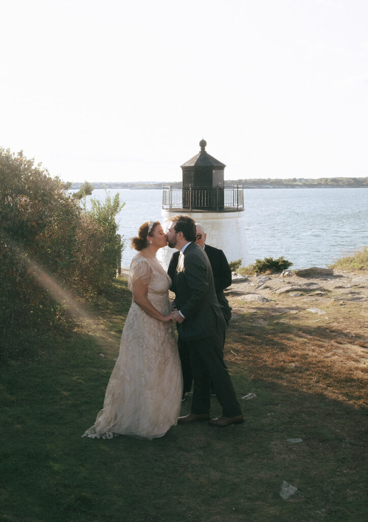 Bride and groom share their first kiss as a married couple in front of the Castle Hill Lighthouse on their wedding day. Photo by Rhode Tripper Photography