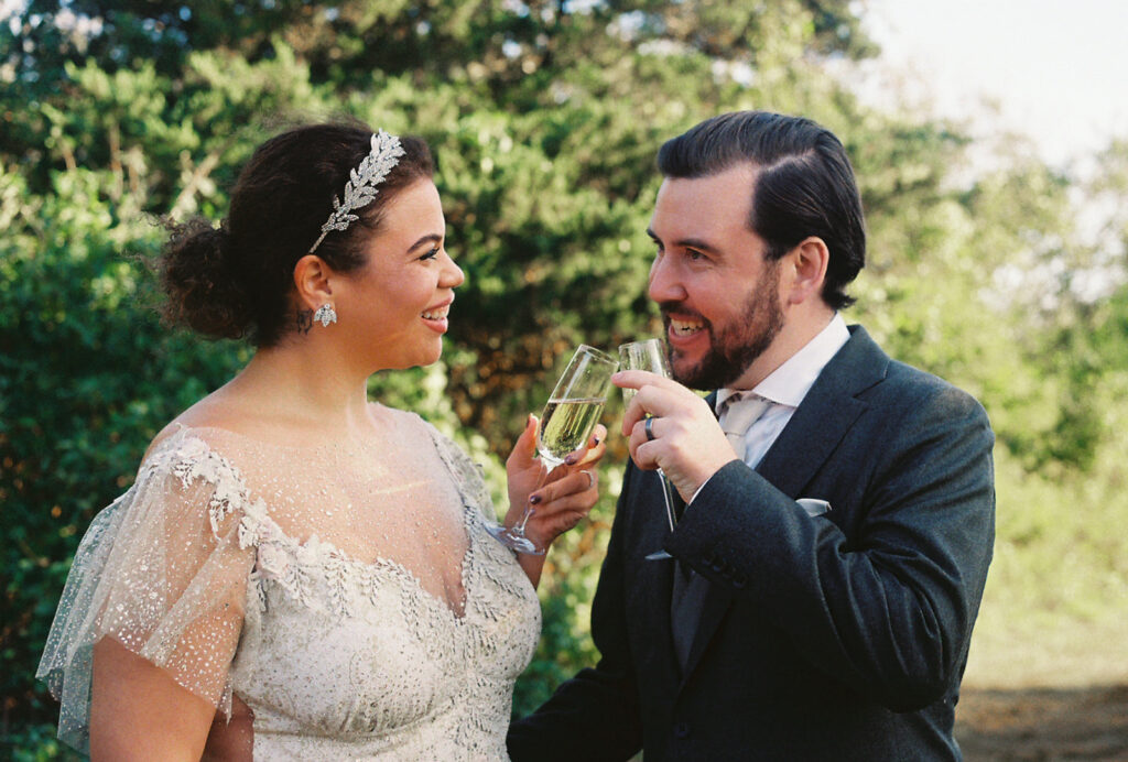 Bride and groom smile and cheers their champagne flutes post ceremony. Photo by Rhode Tripper Photography