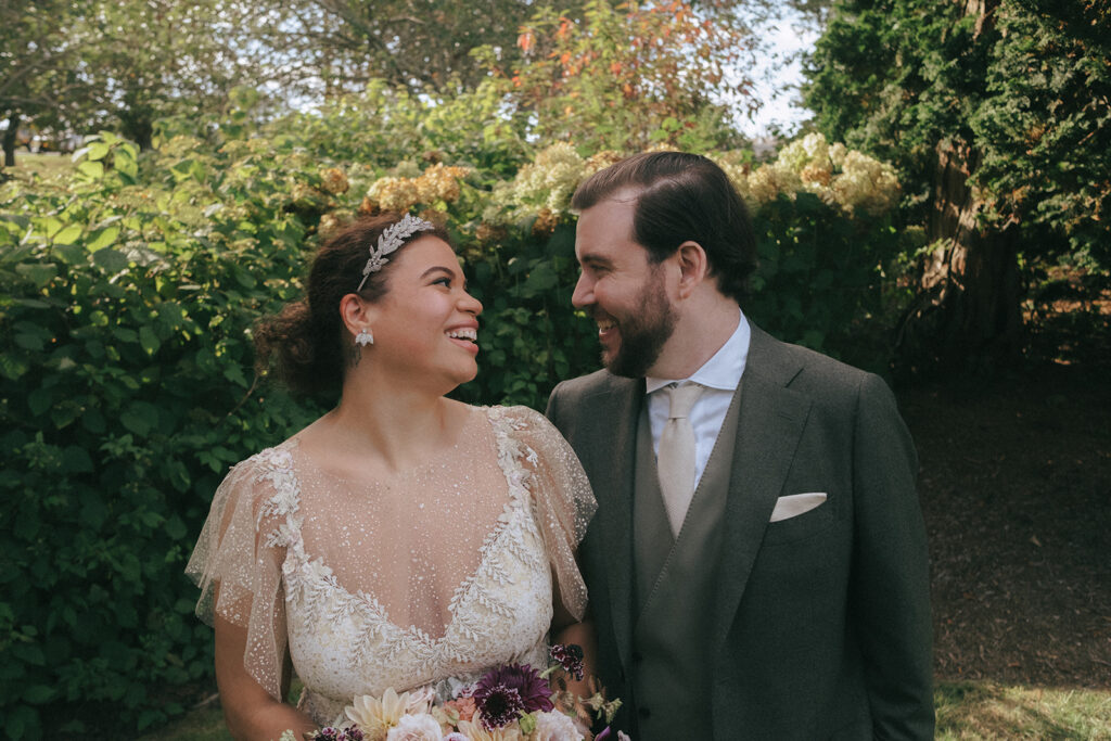 Close up view of bride and groom smiling and looking at each other. Surrounded by greenery at Castle Hill Inn. Photo by Rhode Tripper Photography