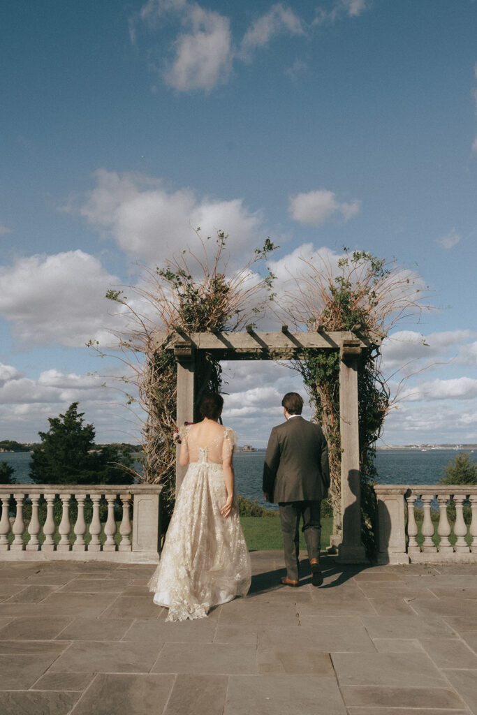 Bride and groom walk towards the pergola portion of the chalet lawn at Castle Hill Inn. Blue skies and fluffy clouds fill the sky. Photo by Rhode Tripper Photography