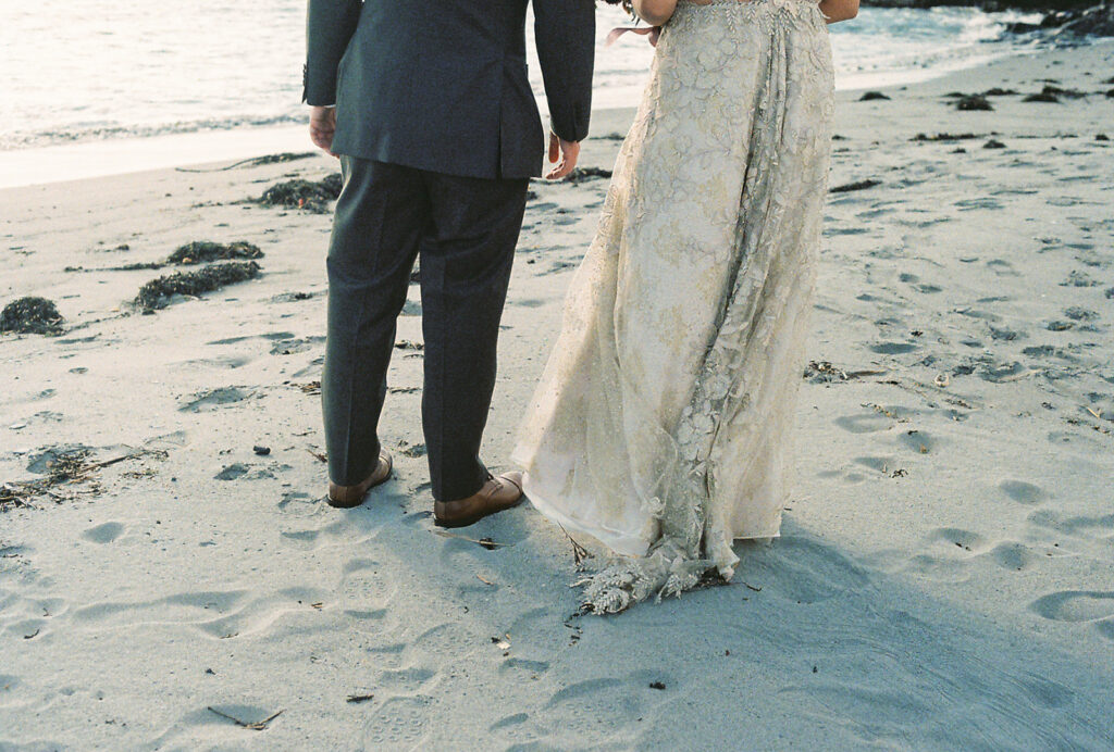 Lower half of bride and groom in the sand on the private beach at Castle Hill Inn. Breeze blowing the bride's lace train. Photo by Rhode Tripper Photography