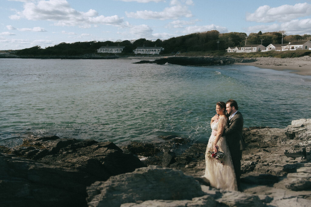 Bride and groom embrace and look out towards the ocean on their wedding day at Castle Hill. Photo by Rhode Tripper Photography