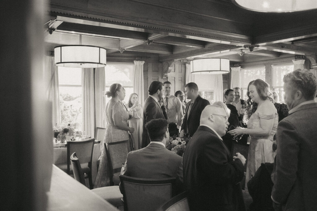 Black and white photo of guests mingling during cocktail hour. Wedding inside the Ocean Room at Castle Hill Inn. Photo by Rhode Tripper Photography