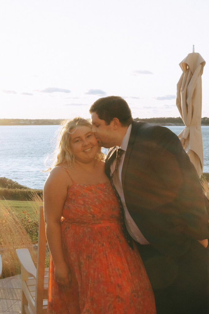 Wedding guests kiss on the patio of Castle Hill Inn with the setting sun behind them. Photo by Rhode Tripper Photography