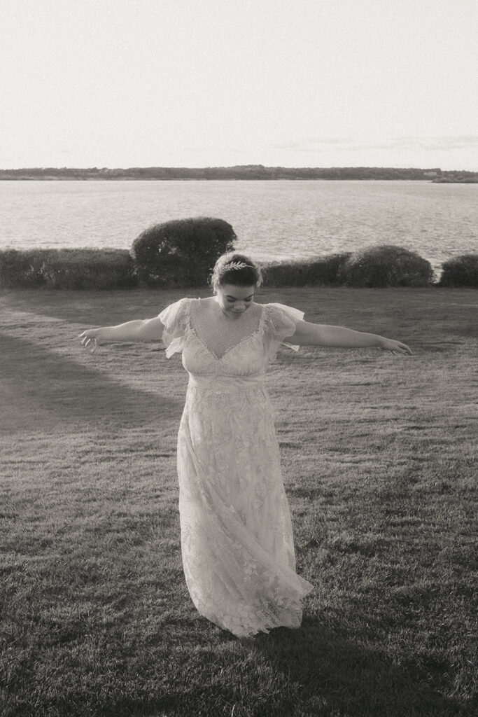 Black and white photo of bride in her lace wedding dress twirling on the Castle Hill lawn. Photo by Rhode Tripper Photography