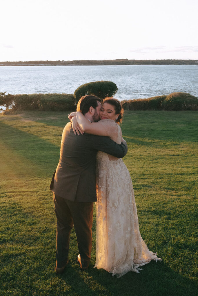 Bride and groom embrace in their wedding attire on the Castle Hill Lawn. Narragansett Bay sits in the background. Photo by Rhode Tripper Photography