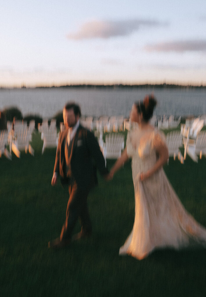 Bride and groom walk across the lawn at Castle Hill at sunset. Light is pink and photo has intentional motion blur. Photo by Rhode Tripper Photography