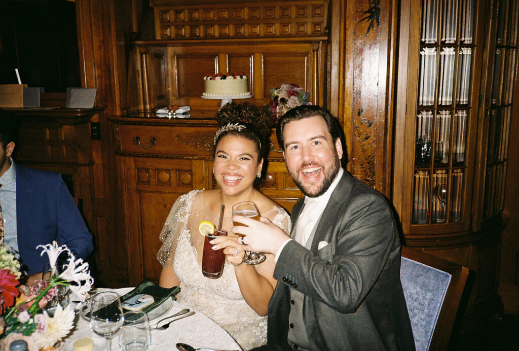 Couple Smiles and Toasts to their wedding while seated at their dinner table. Photo by Rhode Tripper Photography