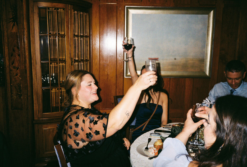 Guests raise a glass to toast the bride and groom during the reception. Located in a wood paneled room in Castle Hill Inn. Photo by Rhode Tripper Photography