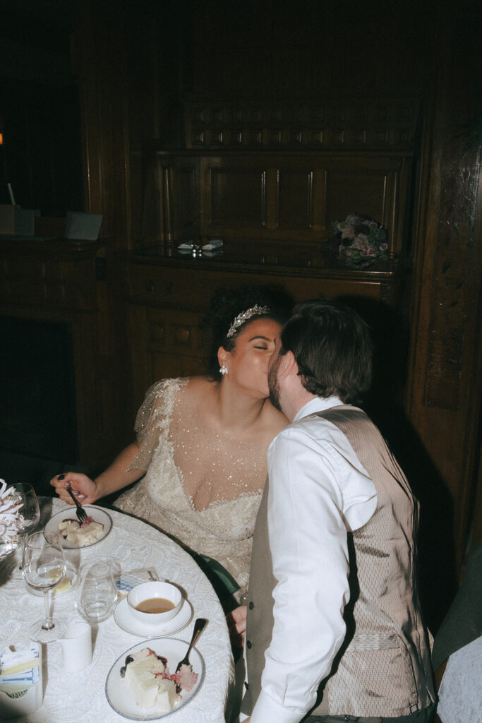 Bride and groom kiss while seated at their reception table for their wedding at Castle Hill. Photo by Rhode Tripper Photography