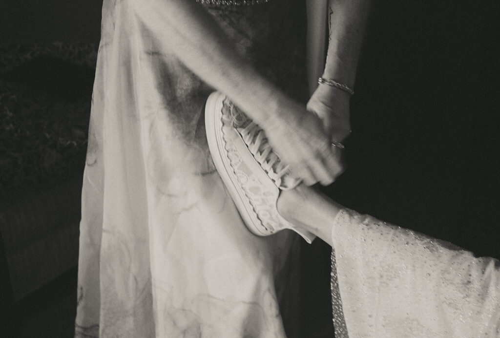 Close up in black and white of the mother of the bride tying the bride's shoe. The bride's foot rests on the mother's leg. Photo by Rhode Tripper Photography