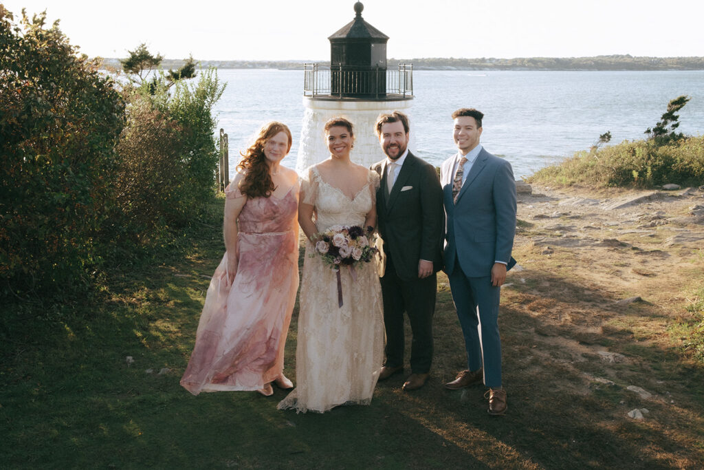 Bride's family poses for a family photo on the lawn with the Castle Hill Lighthouse and bay in the background. Photo by Rhode Tripper Photography