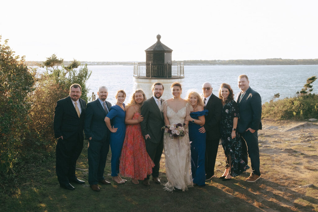 Groom's family smiles and poses for a family portrait in front of Castle Hill Lighthouse. Photo by Rhode Tripper Photography