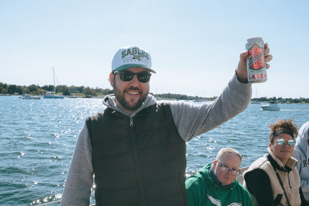 Groom in casual clothing raises a Narragansett Lager to toast to his wedding weekend. Narragansett Bay serves as the background. Photo by Rhode Tripper Photography