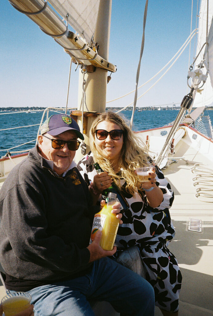 Guests smile looking at the camera with mimosas in hand. Sailing on Narragansett Bay in Newport, RI. Photo by Rhode Tripper Photography