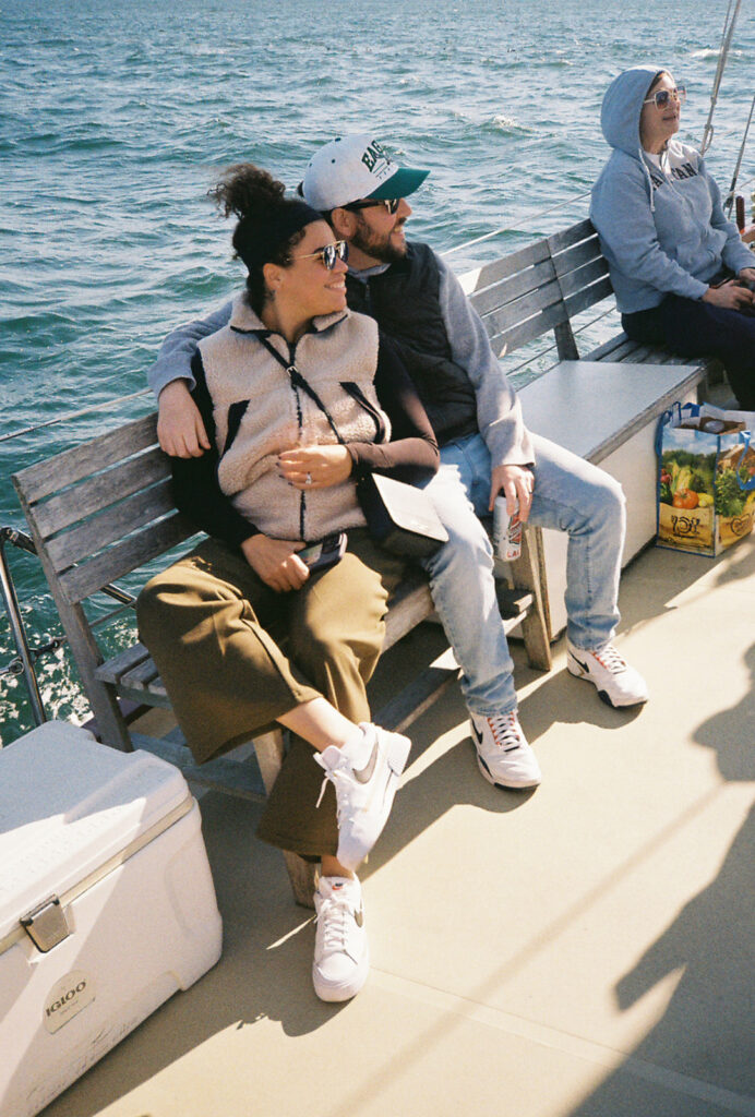 Couple snuggles up into each other while seated aboard the Schooner Aquidneck. Ship is sailing along Narragansett Bay. Photo by Rhode Tripper Photography