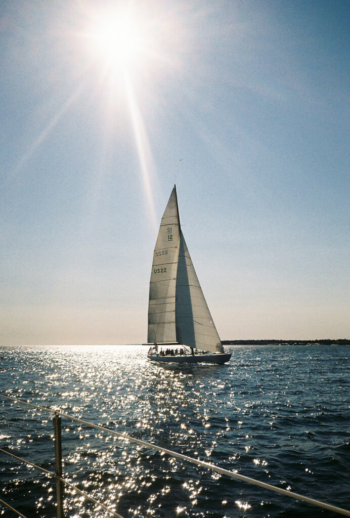 Sun flares in the top of the photos with a large sailboat sitting beneath it. Photo by Rhode Tripper Photography