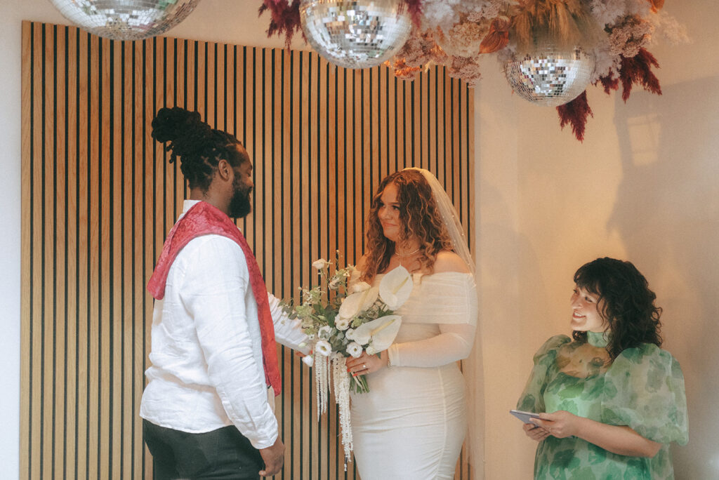 Bride and groom standing at the altar for their Dearly Studio micro wedding ceremony. Officiant and friend Jusmine stands to the side to preside over the ceremony.