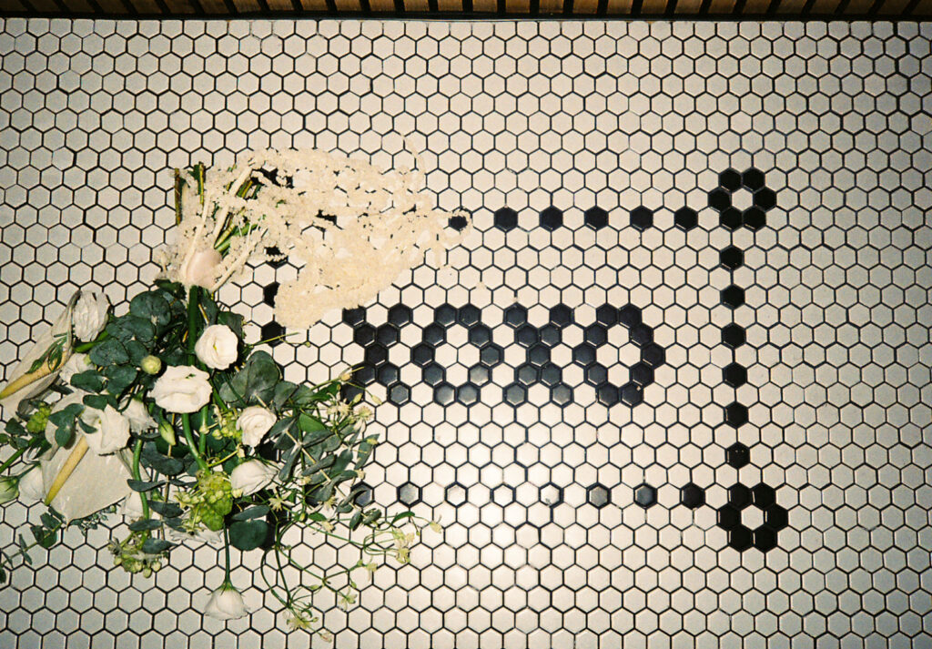 Tiled altar at Dearly Studio that reads "XOXO" in black and white. Bride's bouquet of all white and green florals lays on top of the altar. Captured on film.