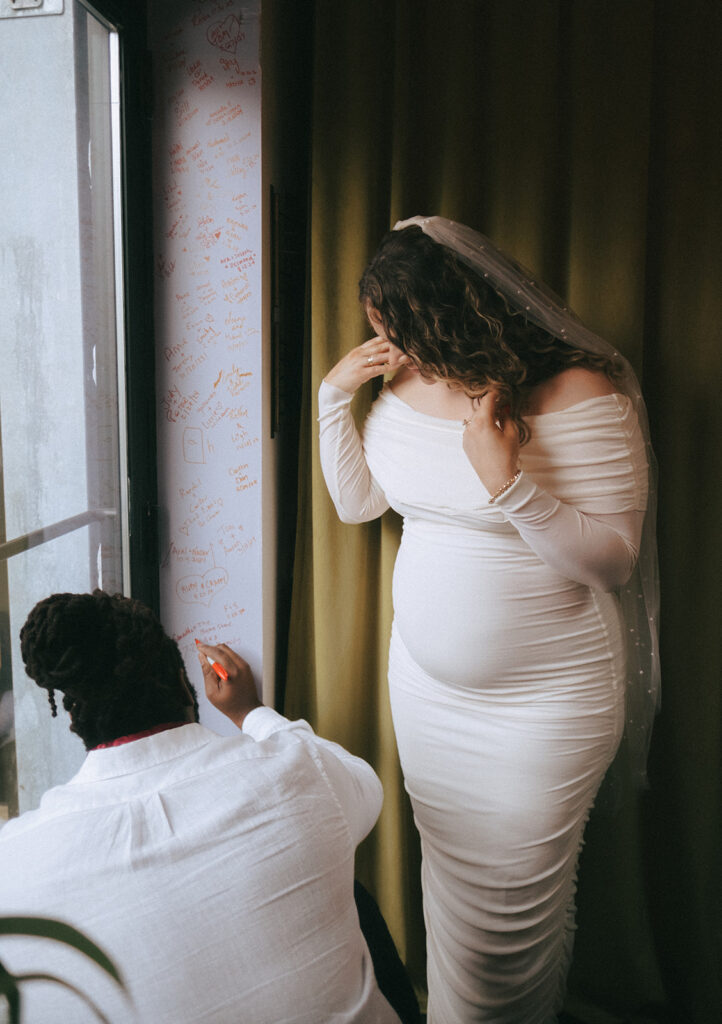 Couple signs the purple door frame at Dearly Studio in red Sharpie to commemorate their micro wedding.