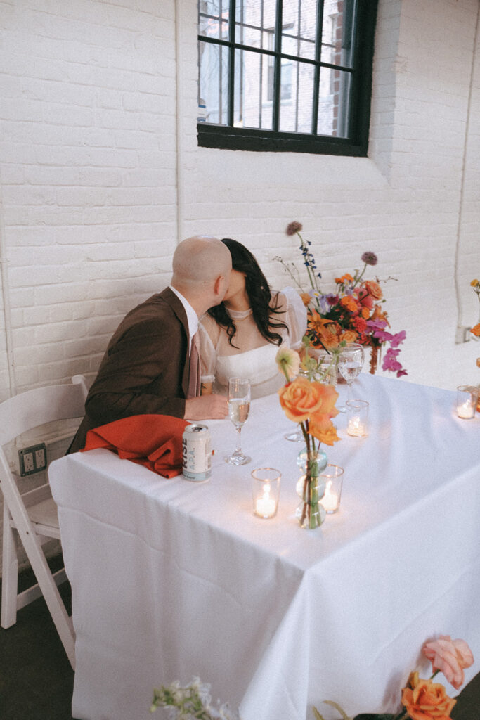 Couple kissing at sweetheart table surrounded by candlelight at their industrial loft reception in Providence. Photo by Rhode Tripper Photography