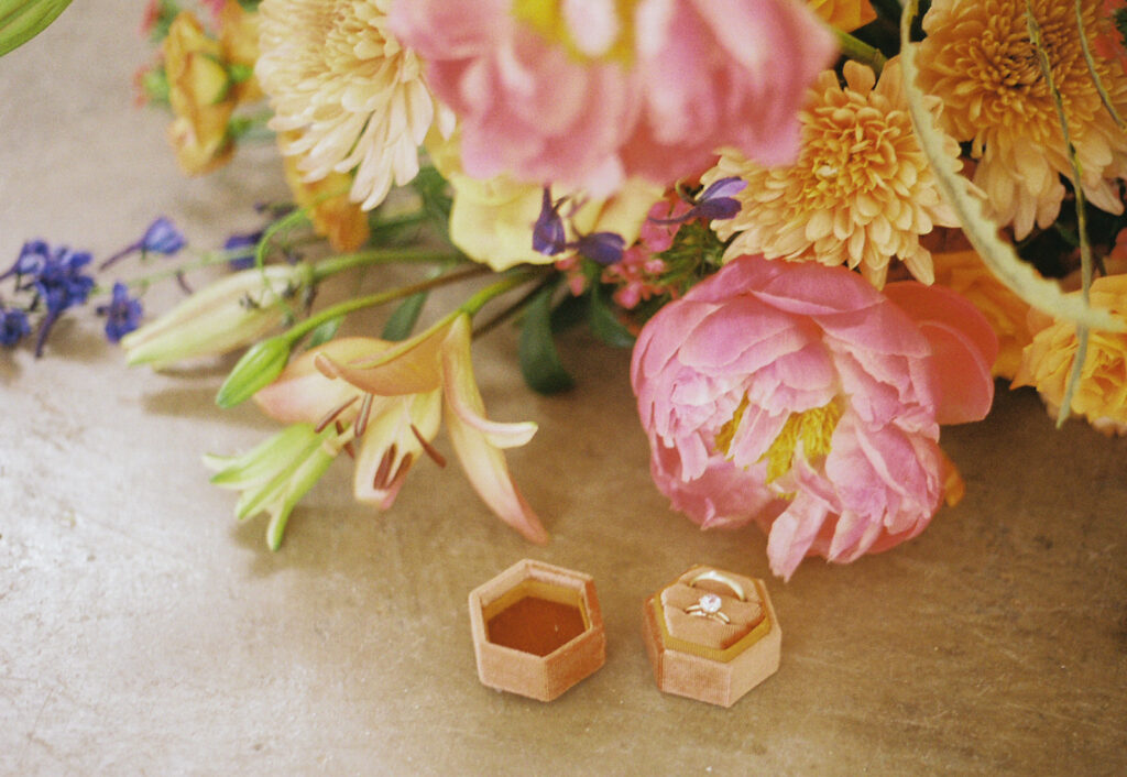 Wedding rings displayed on concrete surface surrounded by colorful florals at boutique hotel spring wedding. Photo by Rhode Tripper Photography