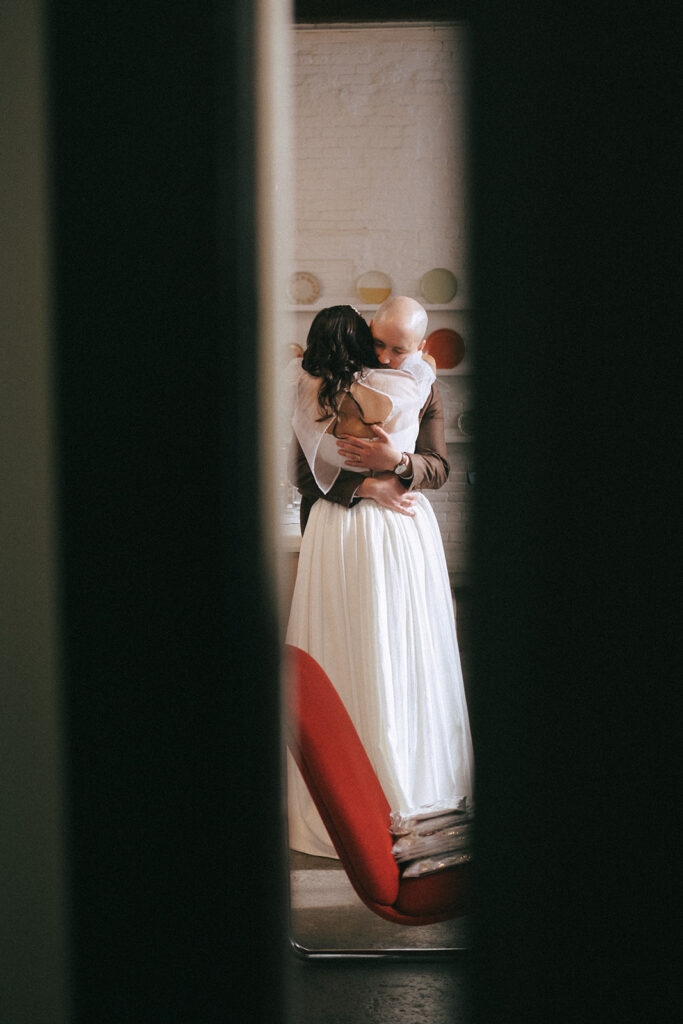 Candid photo through doorway of bride and groom embracing in the Dye House Loft space. Photo by Rhode Tripper Photography