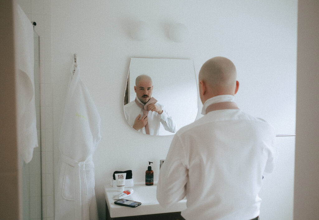 Groom fixing his tie while getting ready at industrial chic hotel loft. Photo by Rhode Tripper Photography