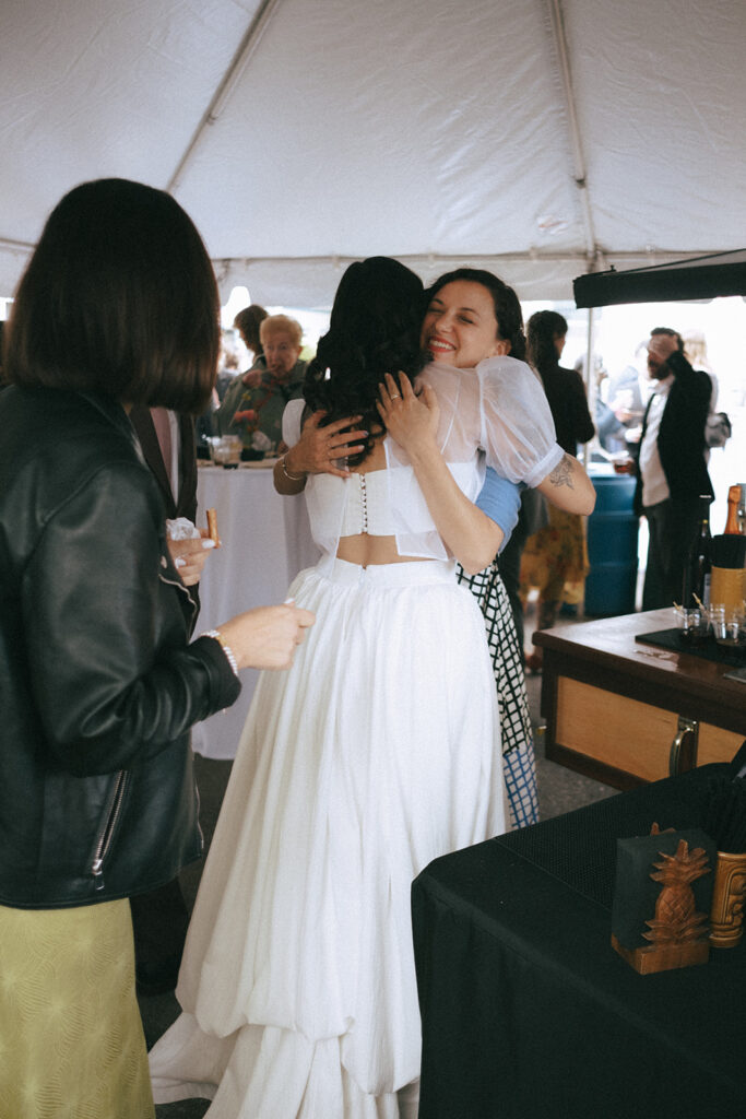 Bride hugging friend during cocktail hour. Photo by Rhode Tripper Photography