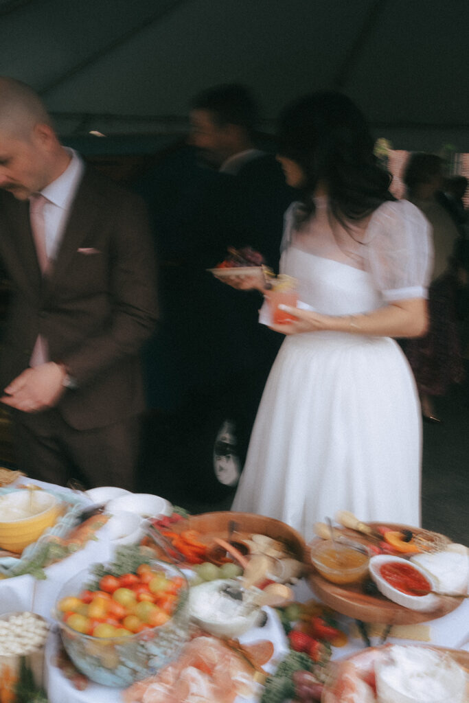 Bride and groom picking at a grazing table at spring wedding cocktail hour. Photo by Rhode Tripper Photography