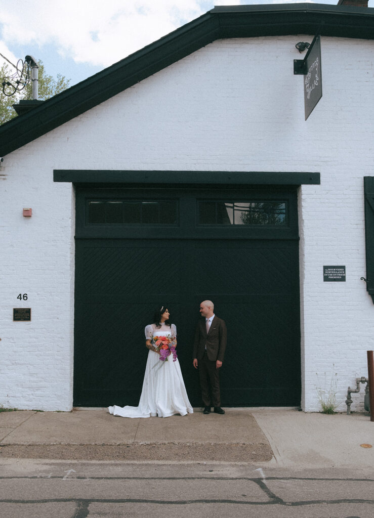 Bride and groom with bright spring flowers against black garage door at boutique hotel wedding in Providence. Photo by Rhode Tripper Photography