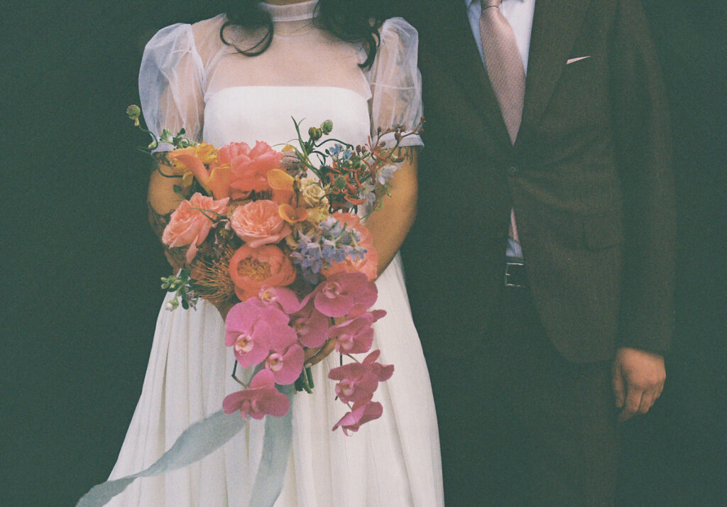 Spring bride holding colorful bouquet with groom at boutique hotel venue. Film Photo by Rhode Tripper Photography