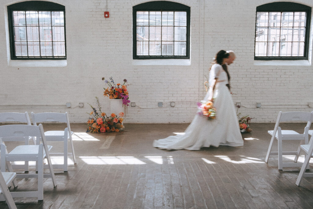 Bride and groom walking past sunlight streaming through windows at boutique hotel ceremony space during spring wedding. Photo by Rhode Tripper Photography