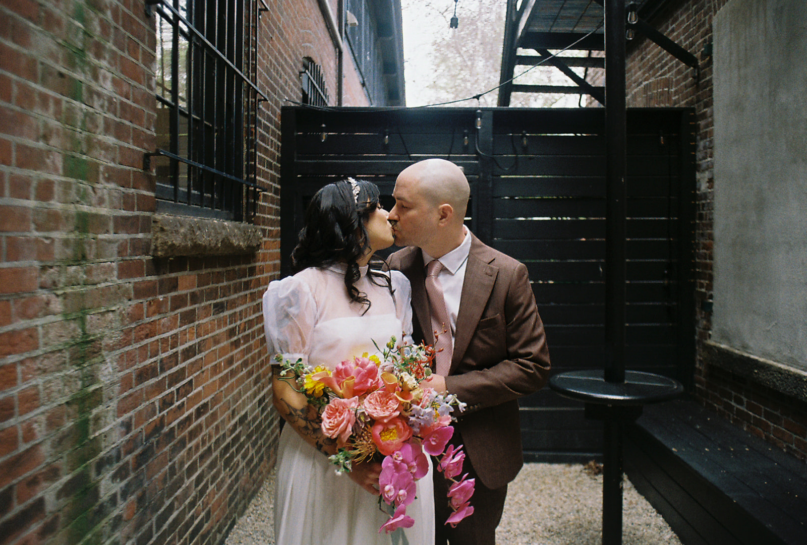 Bride and groom kissing against brick exterior of boutique hotel wedding venue. Photo by Rhode Tripper Photography