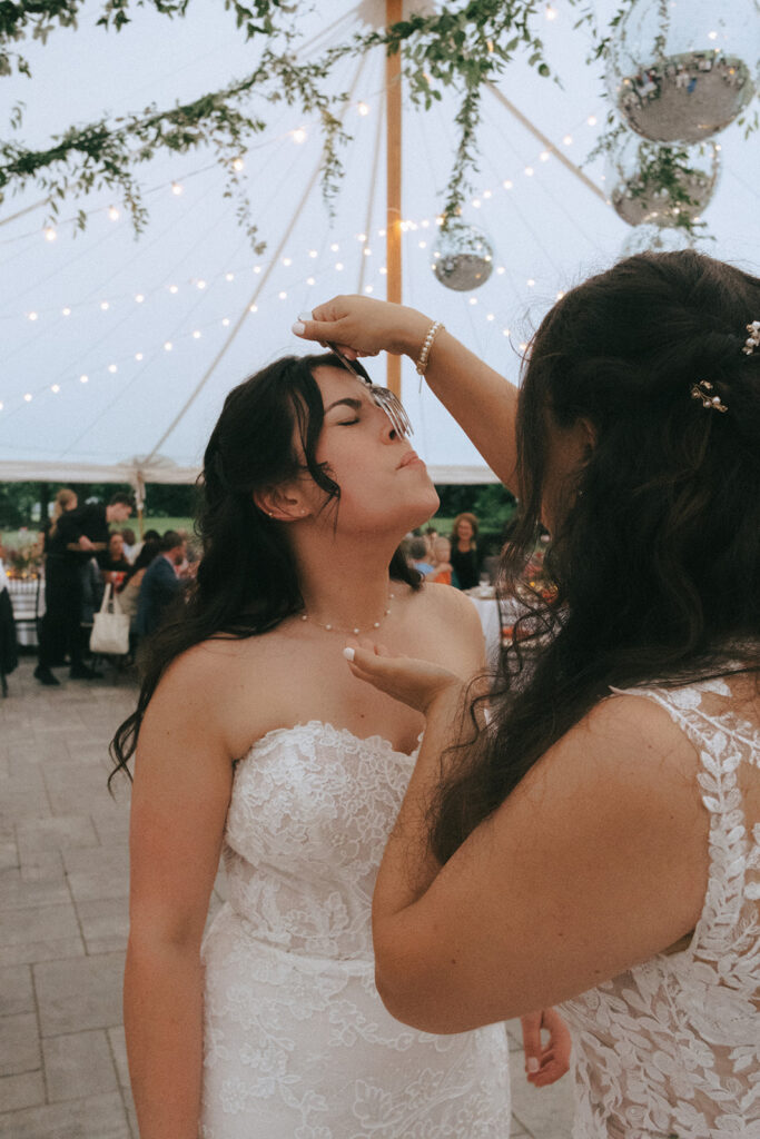 Brides cutting their cake and eating it under the tent at Bradley Estate on their wedding day.